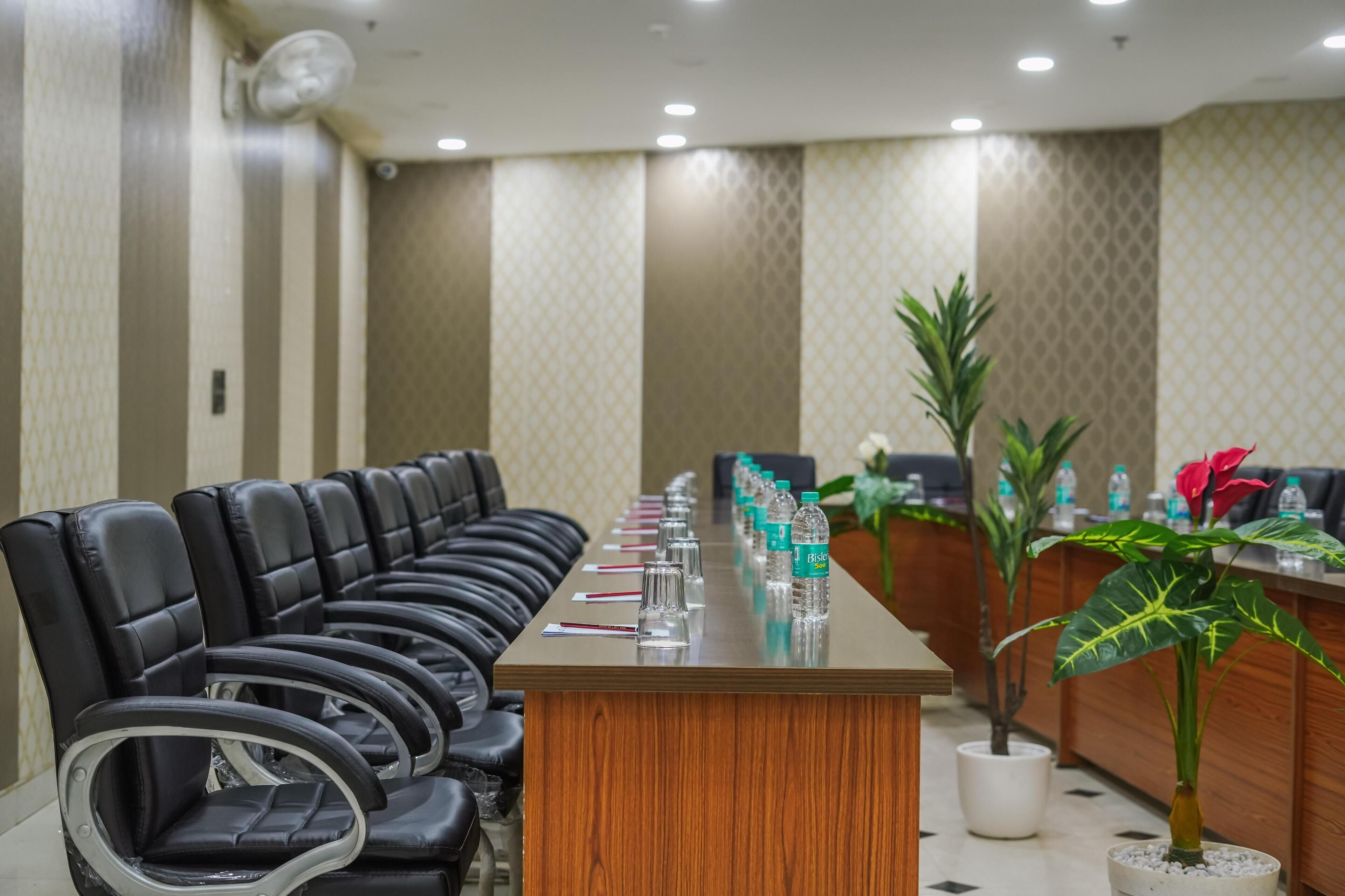 A conference room with a long table, black leather chairs, and a reception desk with plants and water bottles.
