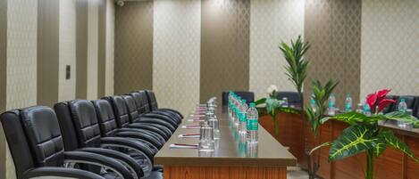A conference room with a long table, black leather chairs, and a reception desk with plants and water bottles.