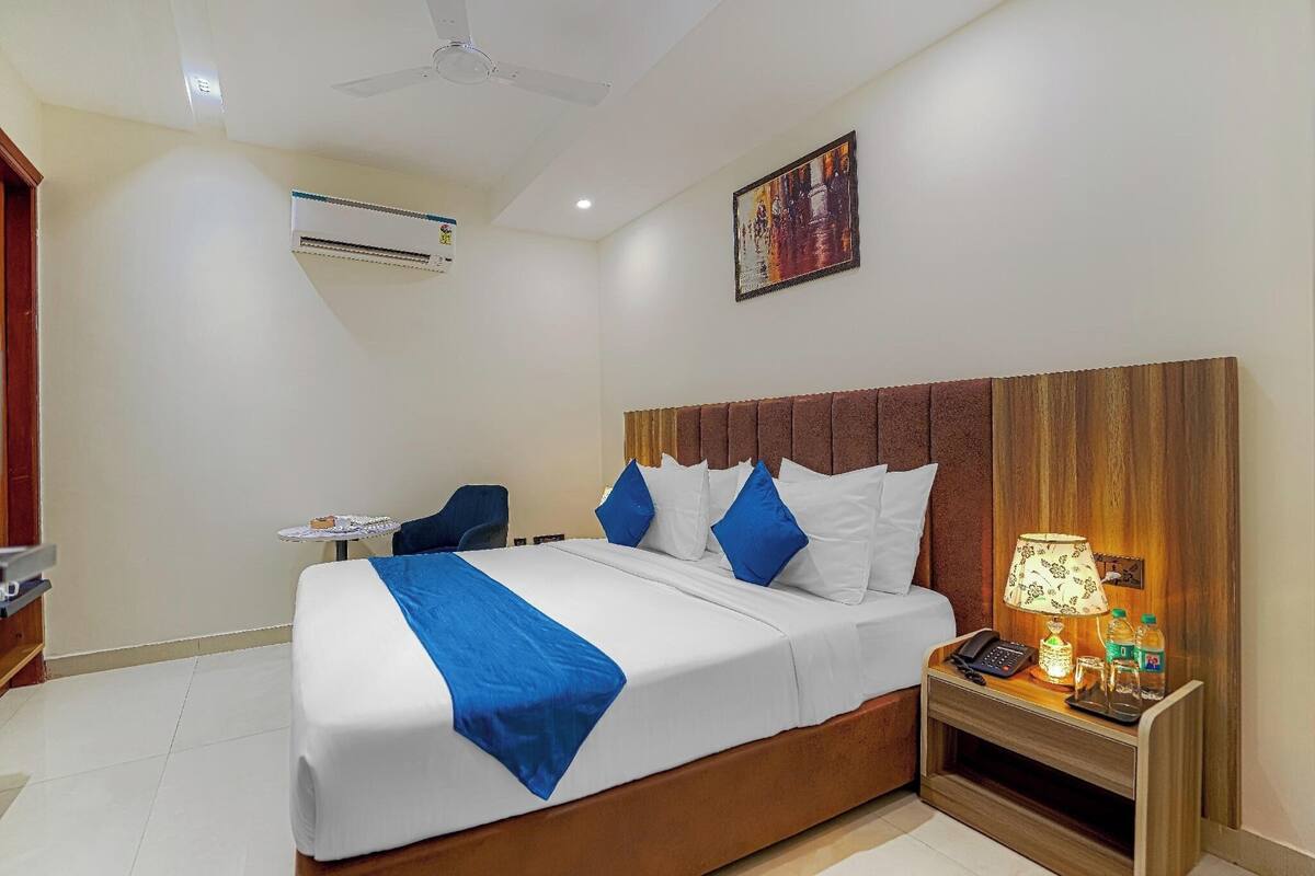 A hotel room with a bed, bedside table, lamp, and air conditioning unit.