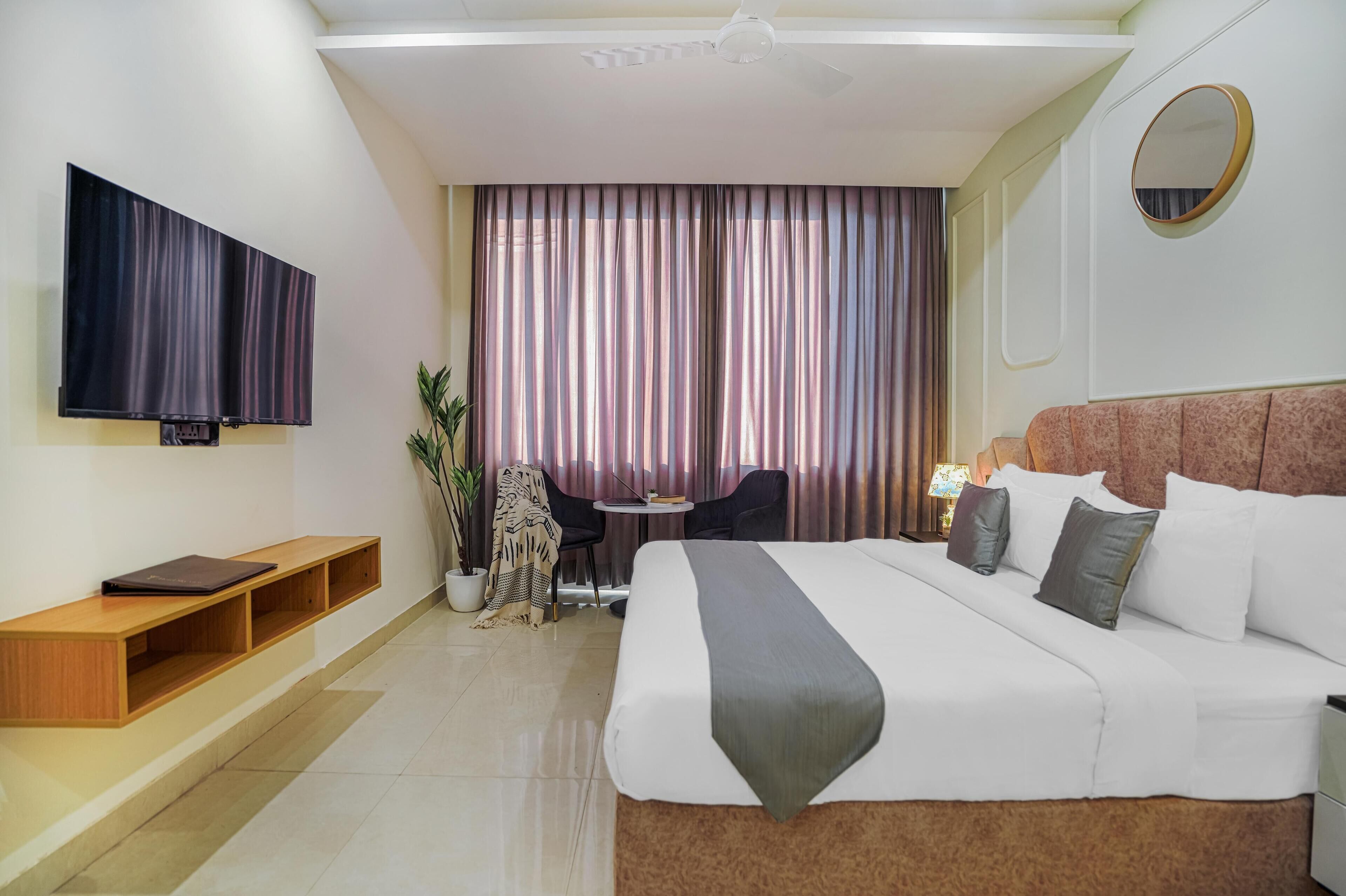 A hotel room with a large bed, a TV mounted on the wall, a small table with chairs, and a potted plant.