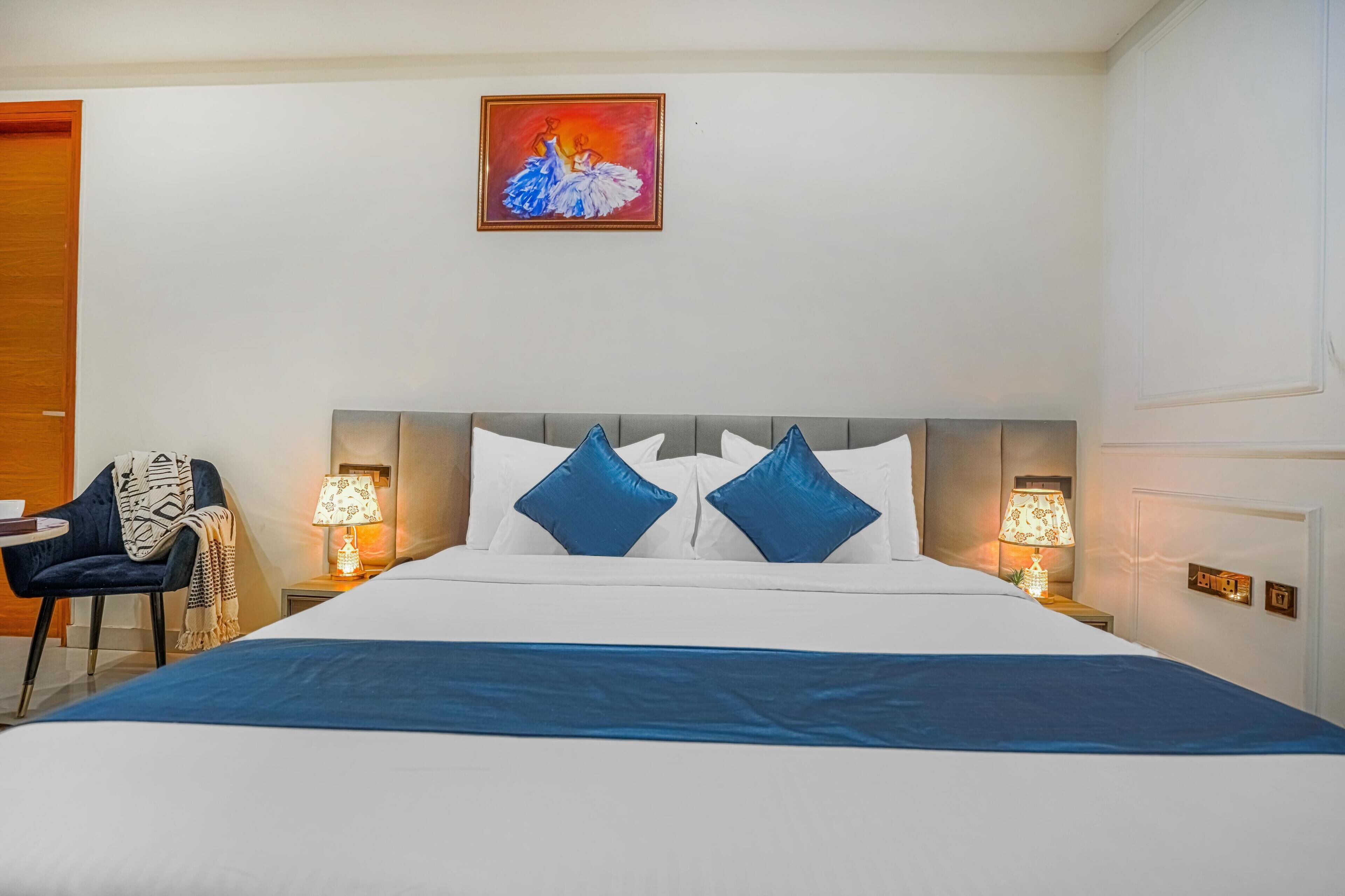 A hotel room with a large bed, two bedside lamps, a chair, and a painting on the wall.