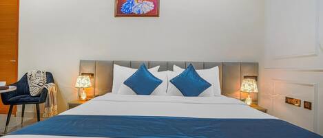 A hotel room with a large bed, two bedside lamps, a chair, and a painting on the wall.