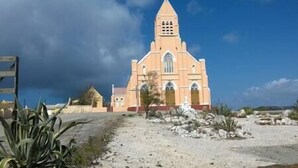 Eine Kirche mit einem Spitzspitzboden und Bogenfenstern, umgeben von Felsen und spärlicher Vegetation.