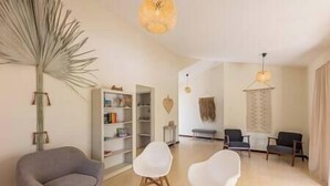 Ein modernes Wohnzimmer mit einem grauen Sofa, zwei weißen Sesseln, einem runden Couchtisch und einem Bücherregal.