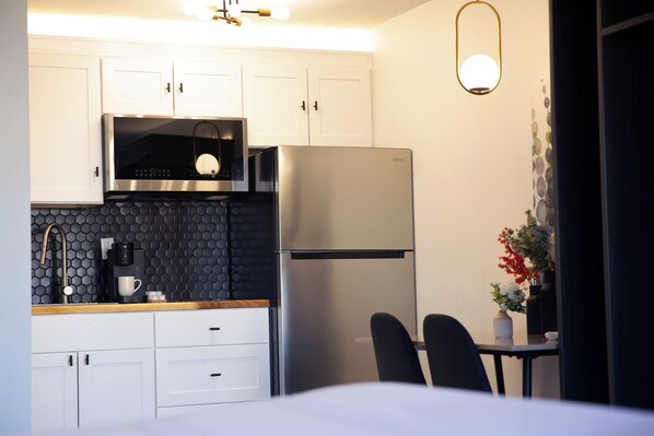 A modern kitchen with white cabinets, a stainless steel refrigerator, a coffee maker, and a black hexagonal backsplash. - The Irish Inn Boutique Hotel (Shamrock)