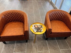 Two brown leather armchairs with quilted backs and metal studs, placed on a tiled floor with a small round table between them.
