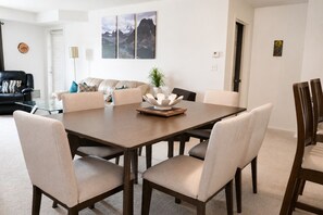 Un comedor con una mesa y sillas de madera, una planta en maceta y un cuadro de un paisaje montañoso en la pared.