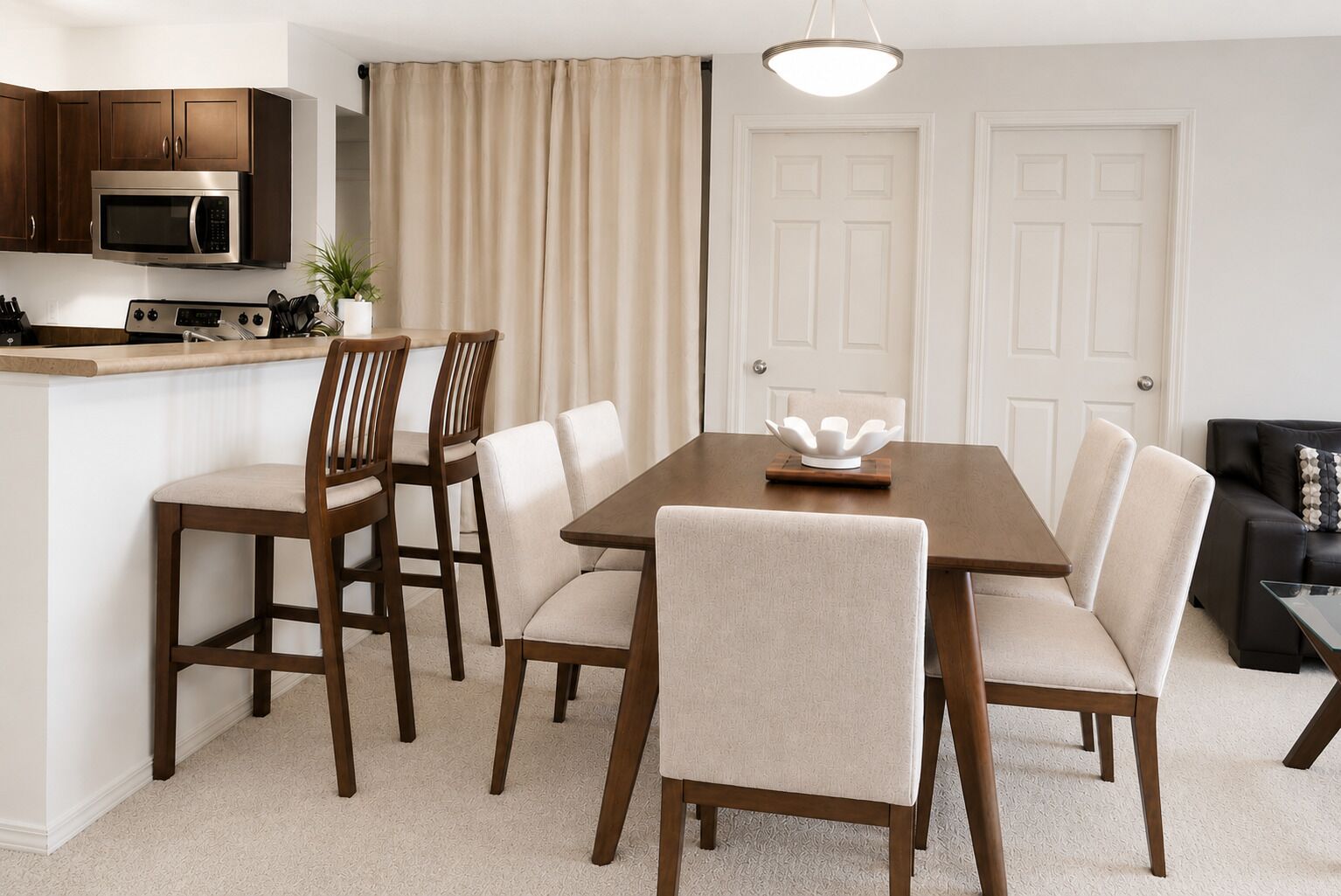 A dining area with a wooden table and chairs, a kitchen with a microwave, and a white door.