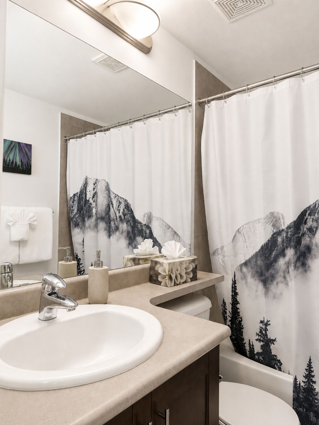A bathroom with a sink, mirror, towel rack, and a shower curtain with a mountain design.