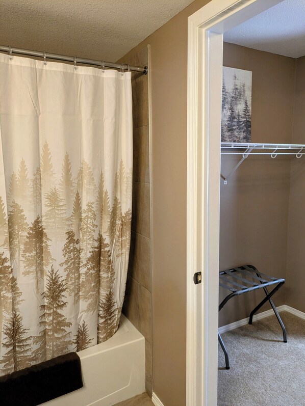 Un baño con cortina de ducha con estampado de bosque, una bañera y un vestidor con una estantería metálica.