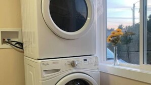 A stacked washer and dryer unit in a laundry room with a window view. - The Guesthouse (Great Falls)
