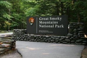 A sign for Great Smoky Mountains National Park with a stone wall and wooden fence in the background.