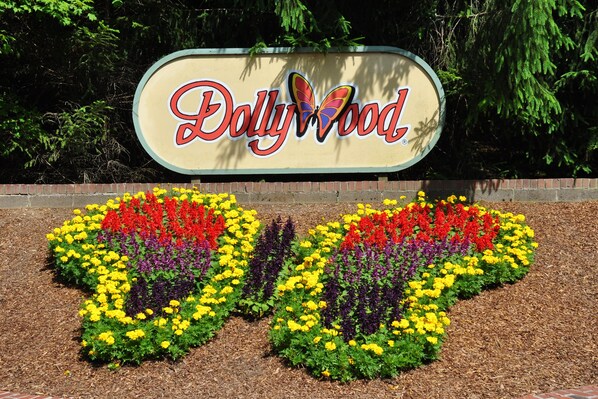 A sign for Dollywood with a colorful flower bed in the shape of a heart.