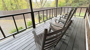 Een houten terras met een leuning, een overdekte ruimte en uitzicht op bomen en een tuin.
