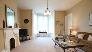 Un salon avec une cheminée, un téléviseur, une table basse en verre, un canapé et un lustre.