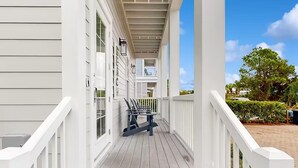 Un portico coperto con pavimento in legno e ringhiere bianche, che conduce a un balcone al secondo piano con ringhiera.