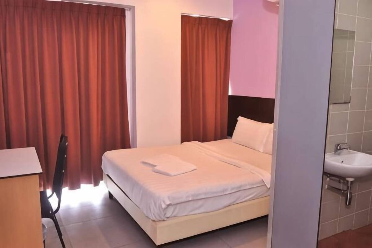 A hotel room with a bed, a desk, a chair, a sink, and a mirror.