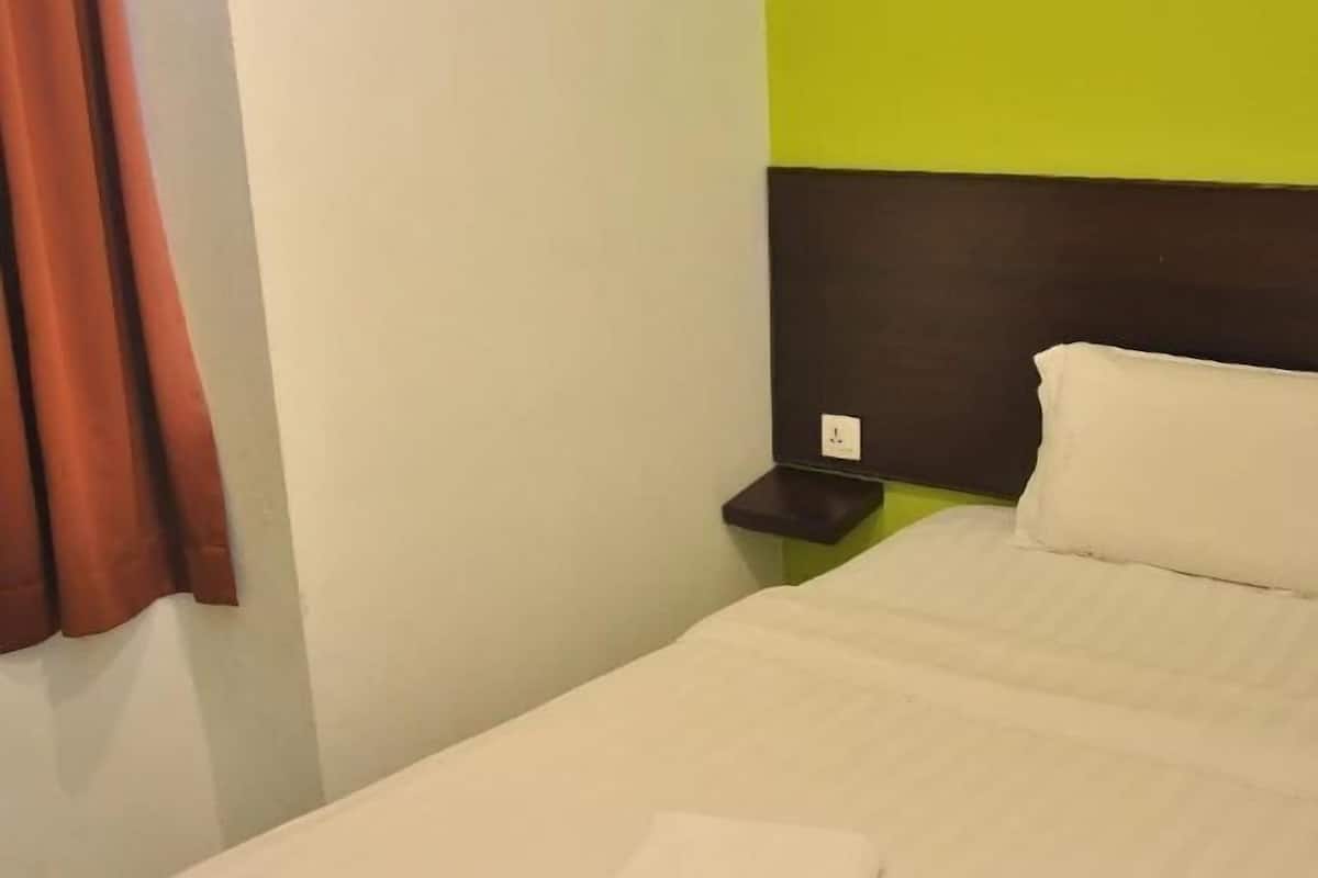 A single bed with a white mattress and pillows, a brown headboard, and a small shelf with a power outlet.