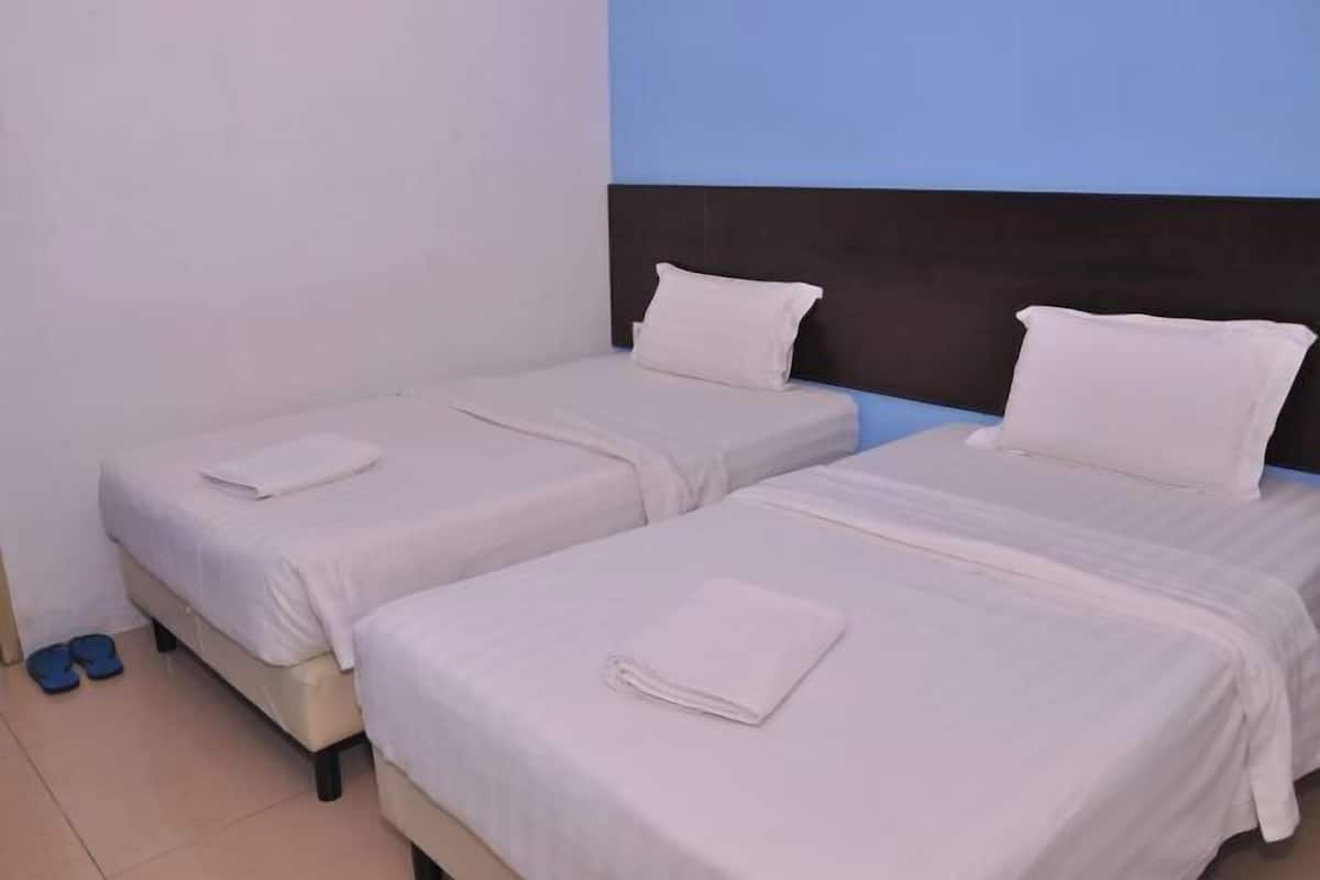 A hotel room with two single beds, each with a white bedspread and pillow, and a dark headboard.