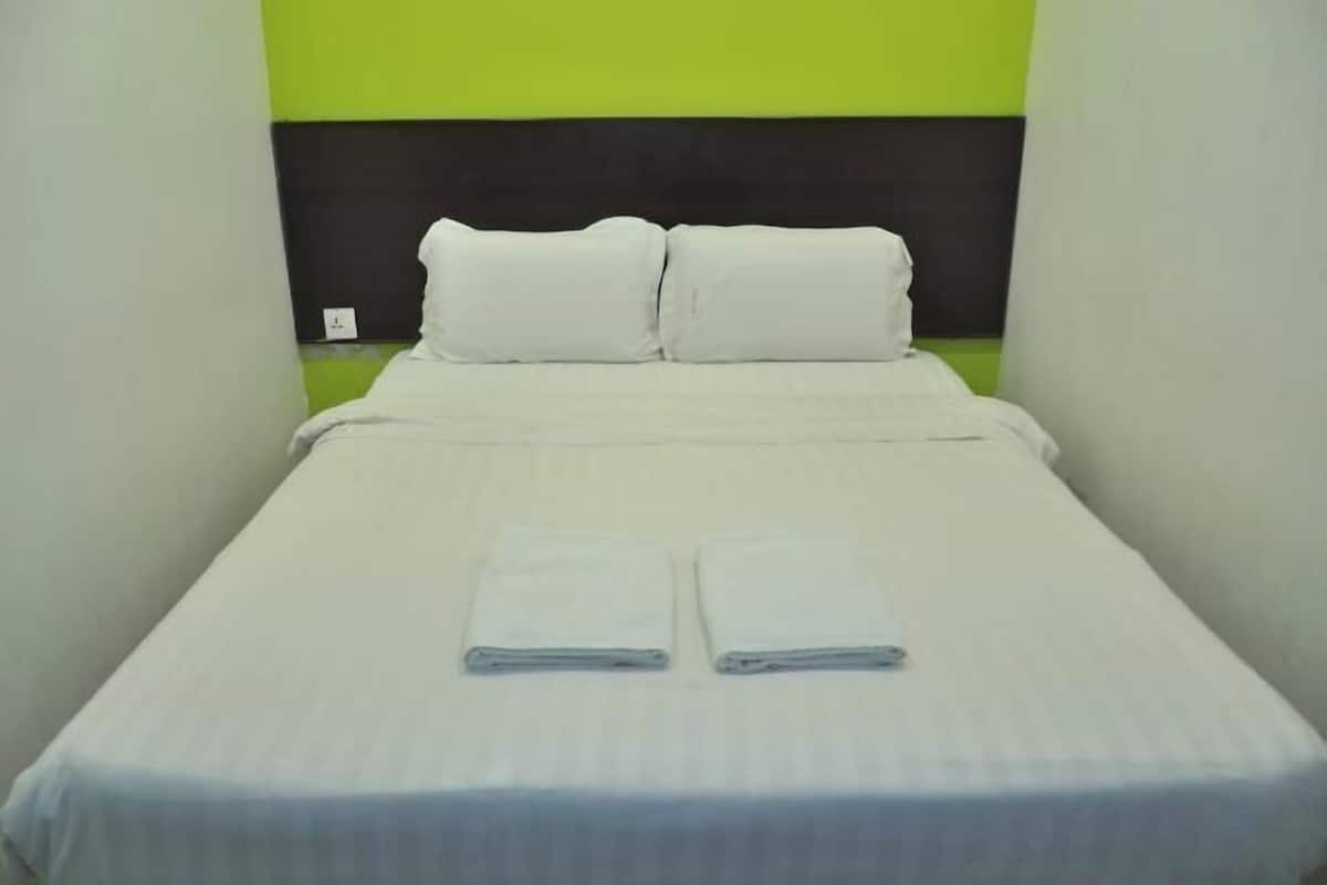 A single bed with white bedding and pillows, a green accent wall, and a black headboard.
