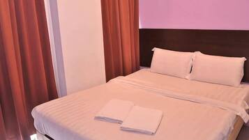 A neatly made bed with white linens and two towels, a dark headboard, and red curtains.