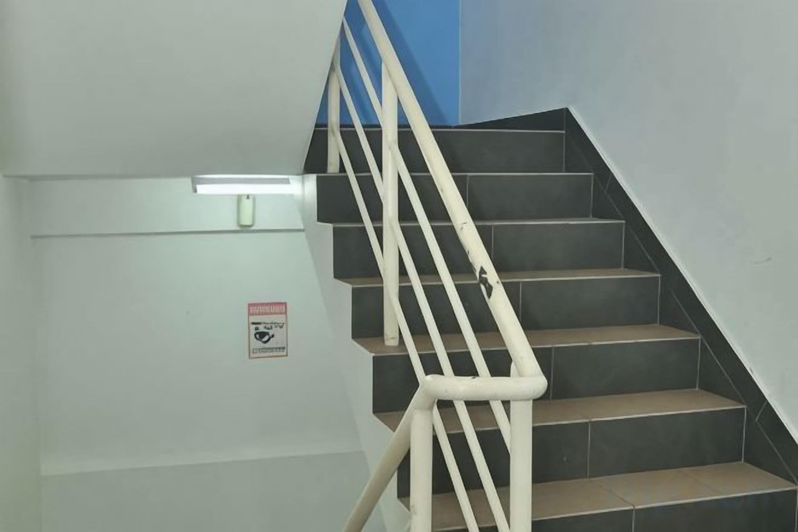 A staircase with a handrail, a light fixture, and a warning sign on the wall.
