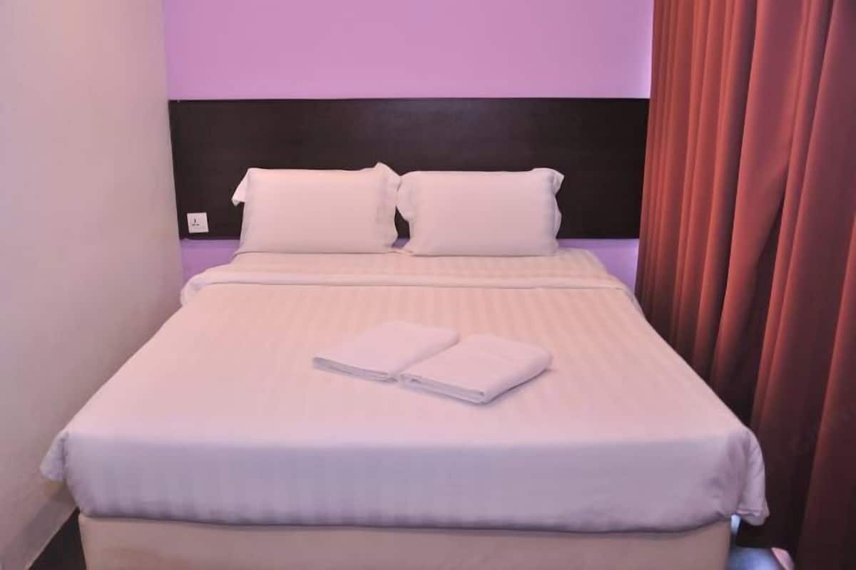 A neatly made bed with white linens and pillows, a folded towel on the bed, and a dark headboard.