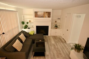 Una sala de estar con sofá, mesa de centro, chimenea y estanterías con plantas.
