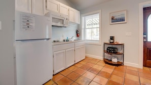 A kitchen with white cabinets, a microwave, a coffee maker, and a window with blinds.