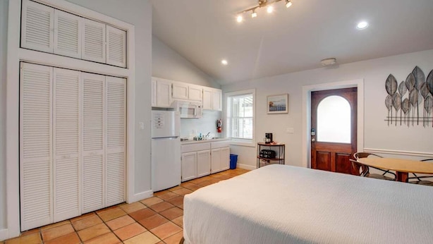A compact bedroom with a bed, a small kitchenette, and a door leading to a bathroom.