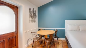 A room with a wooden door, a round table with chairs, a bed with white bedding, and a blue accent wall.