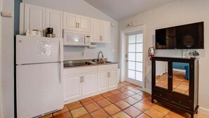 Una cucina compatta con mobili bianchi, un forno a microonde, un frigorifero e un piccolo pensile nero con un televisore.