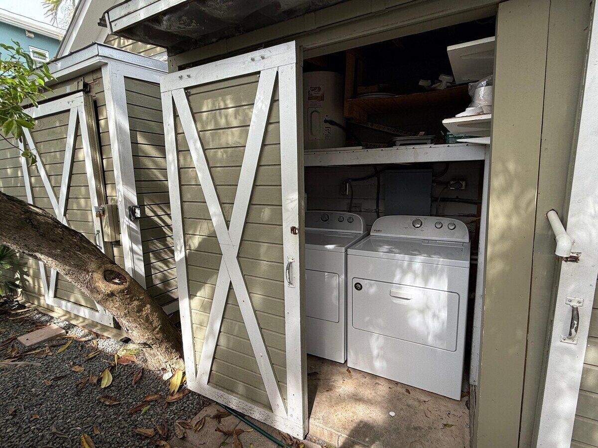 A laundry room with two washing machines and a dryer, enclosed by a wooden fence with a cross-brace design.