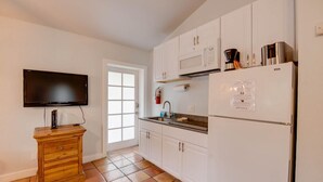 A kitchen with white cabinets, a microwave, a refrigerator, a wooden cabinet, and a television. - Pelican Suite | Cozy Cottage, Hot Tubs, Close to D (Key West)