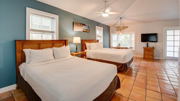 A hotel room with two beds, a ceiling fan, a TV, and a window with blinds. - Pelican Suite | Cozy Cottage, Hot Tubs, Close to D (Key West)