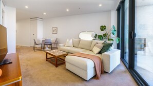 Ein modernes Wohnzimmer mit einer Couch, einem Couchtisch und Sesseln. Ein großes Fenster sorgt für natürliches Licht und einen Ausblick.