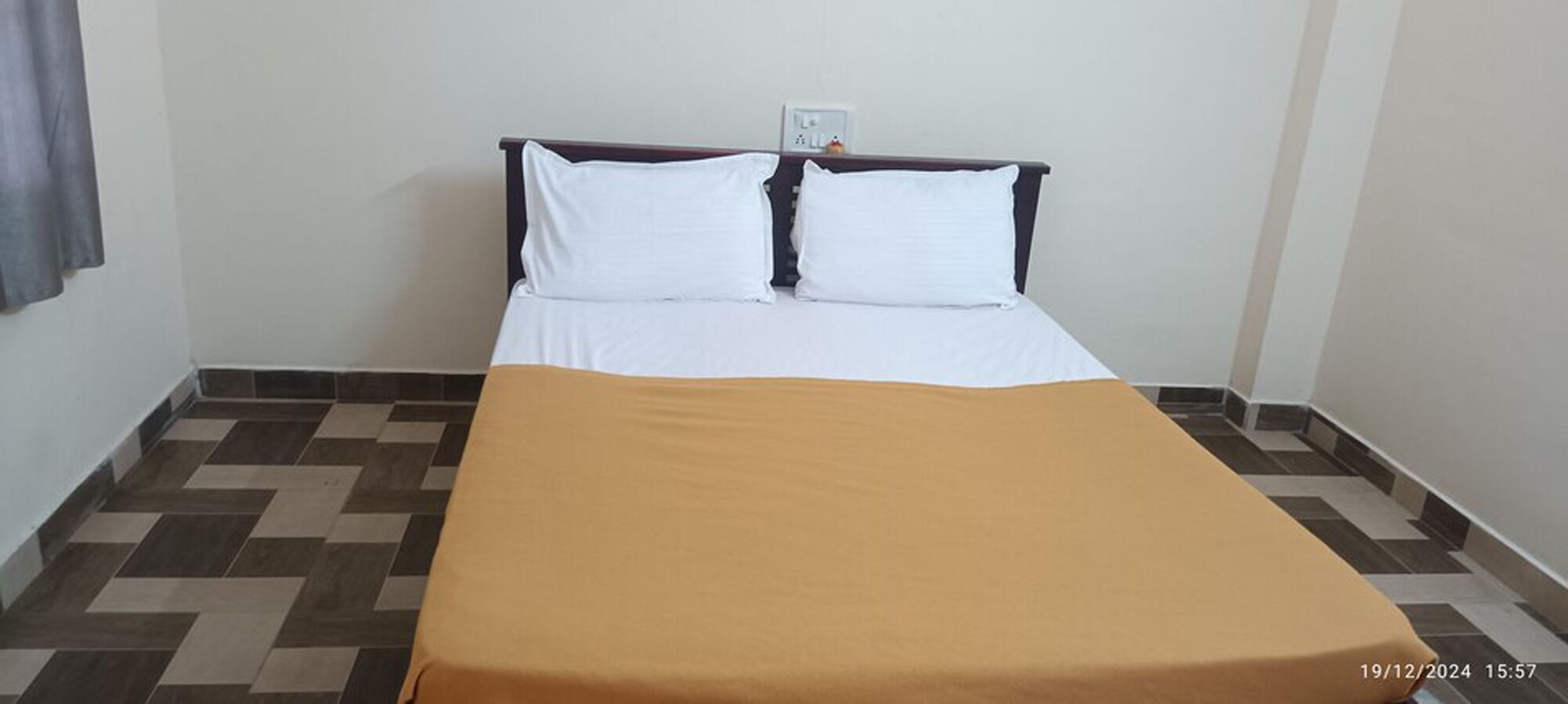 A neatly made bed with a white duvet and two pillows, a brown bedspread, and a checkered floor pattern.
