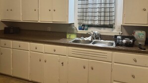 Una cocina con armarios blancos, un lavamanos doble y un ventanal con cortinas a rayas.