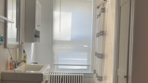 Baño con inodoro, lavabo, radiador y ventana con persianas.