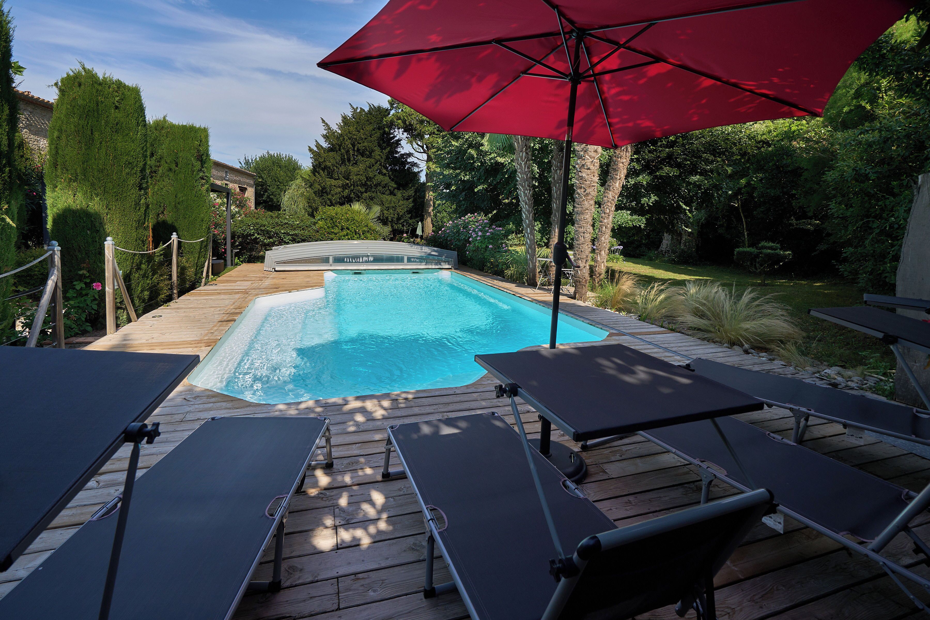 Un terrazzo in legno con piscina, sedie a sdraio e un ombrellone rosso.