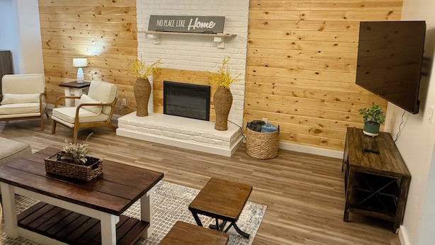 Una sala de estar con chimenea, paneles de madera en las paredes, un televisor montado y un letrero que dice 'No Place Like Home'.