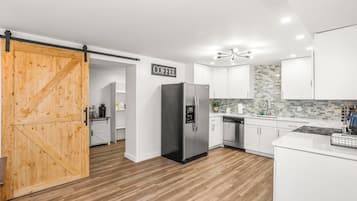 Une cuisine moderne avec des meubles blancs, un réfrigérateur noir et une porte en bois donnant sur un garde-manger.