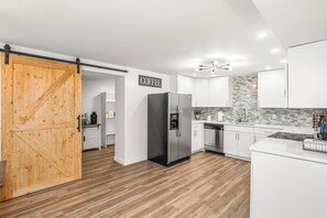 A modern kitchen with white cabinets, a black refrigerator, and a wooden door leading to a pantry.