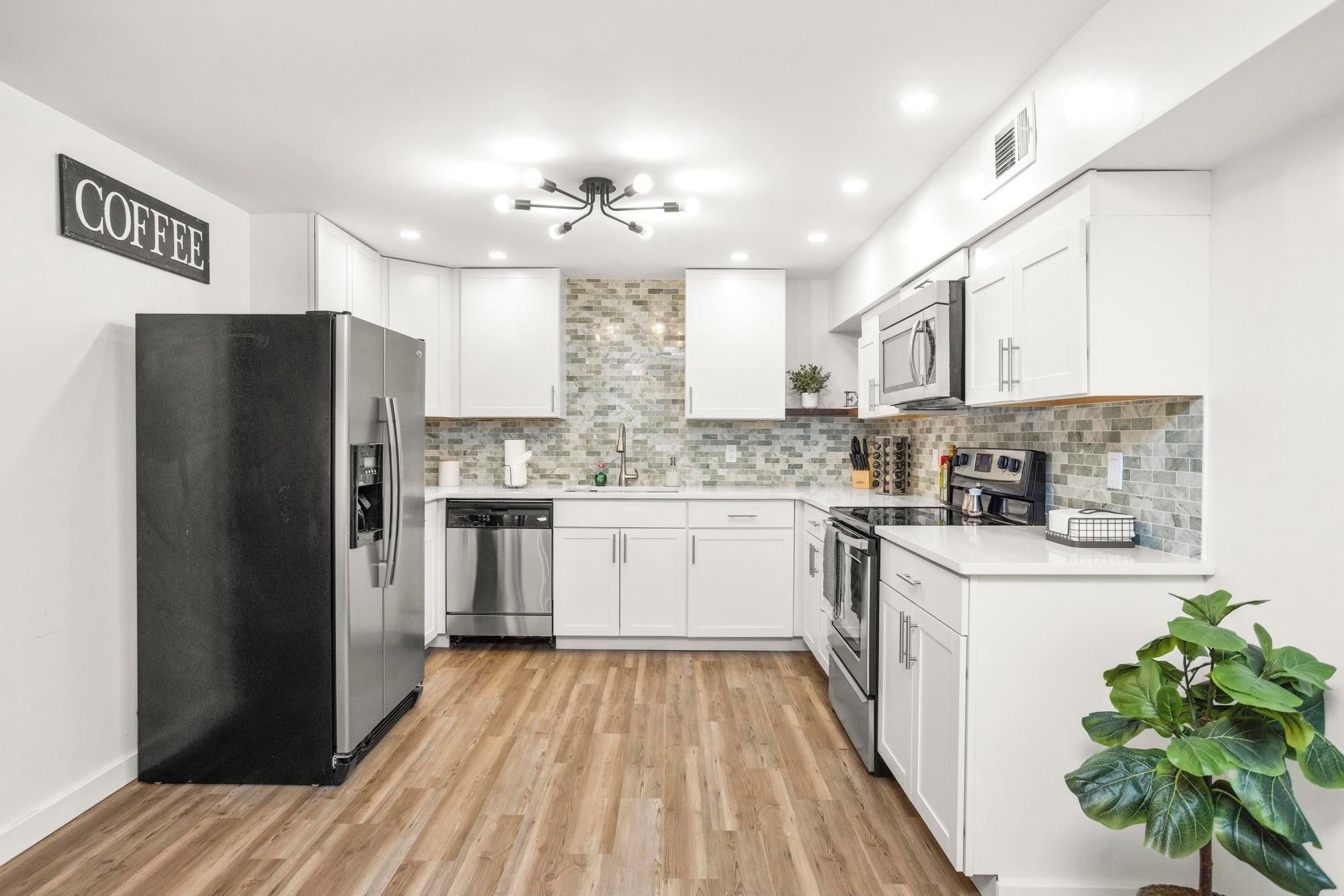 A modern kitchen with white cabinets, a black refrigerator, a microwave, and a coffee sign on the wall.