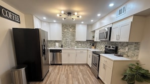 Una cocina moderna con armarios blancos, un refrigerador negro, electrodomésticos de acero inoxidable y piso de madera.