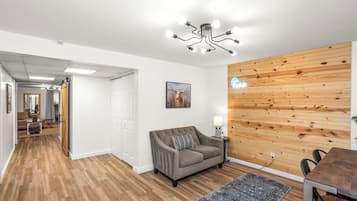Un salon moderne avec un canapé gris, un mur recouvert de panneaux en bois et un luminaire au plafond.