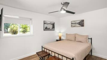 A bedroom with a bed, a ceiling fan, a window, and two wall-mounted pictures.