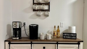 Una cocina con cafetera, tazas y un letrero que dice "Café primero, ustedes después."