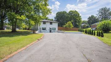 A residential driveway leading to a two-story house with a front yard.