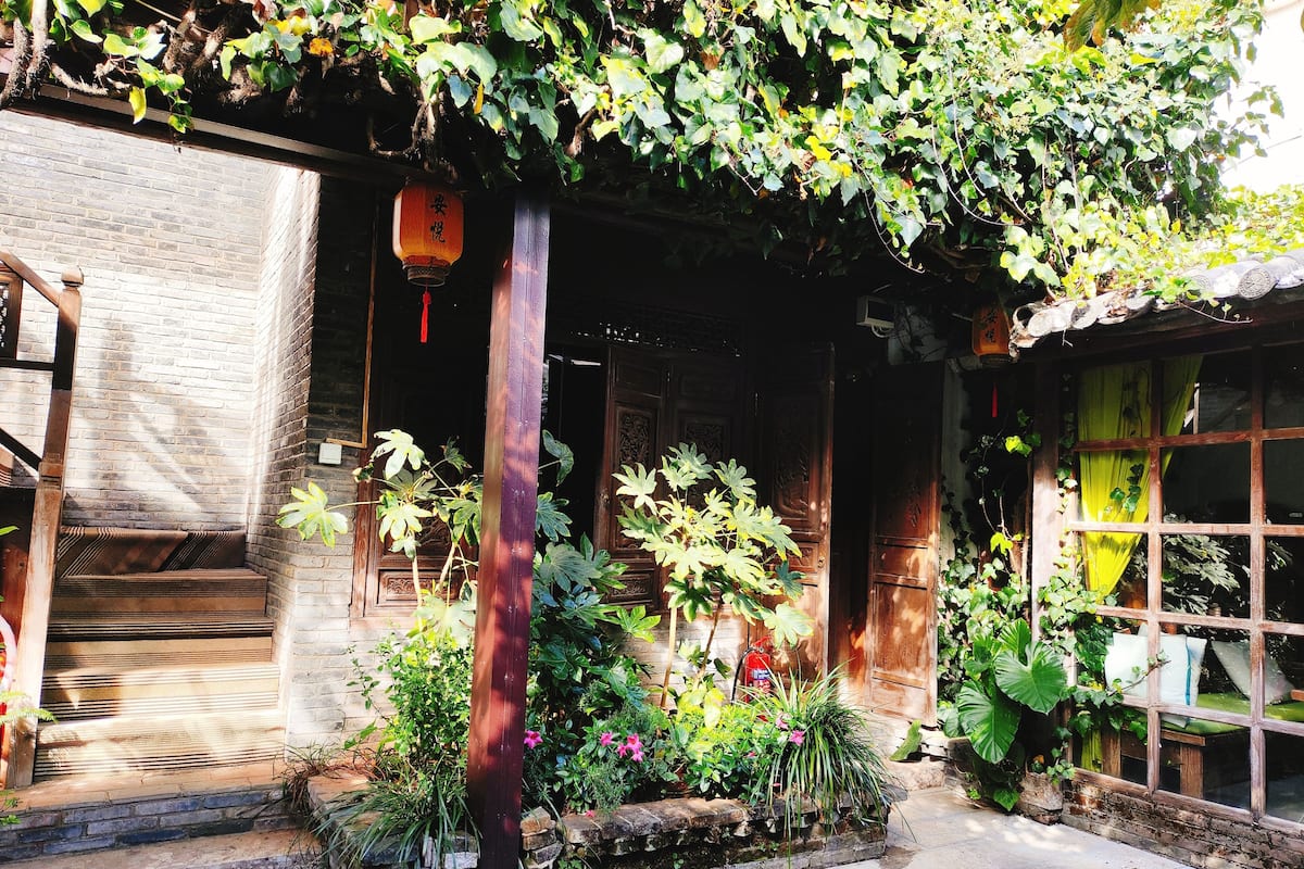 A traditional wooden building with a brick wall, a wooden staircase, and a garden area with various plants and a lantern.